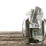 Glass jar with tips on wooden table against white background