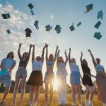 Group of students throwing notebooks in the air celebrating graduation at sunset