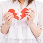 A young friend holding a ripped paper heart after a tough breakup