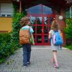 A pair of young students walking into a school, which has been quietly taken over by major corporations