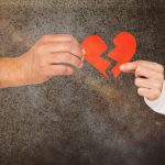 A couple breaking up and splitting a paper heart in half