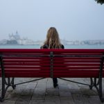Blonde girl on park bench looking at water