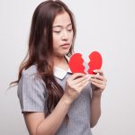 Young woman with paper broken heart.