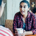 A young woman telling her personal secrets to a friend at a coffee shop