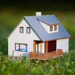 A small model home in the green grass, possibly covered by a warranty