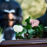 Someone placing flowers on a casket at a funeral