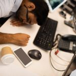 A tired man at his desk who is overworking, an unhealthy coping mechanism