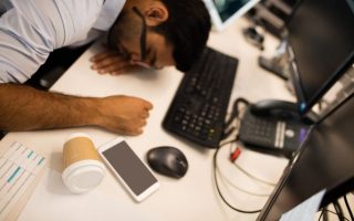 A tired man at his desk who is overworking, an unhealthy coping mechanism