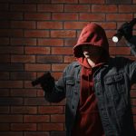 A criminal with a gun and flashlight looking for a new victim